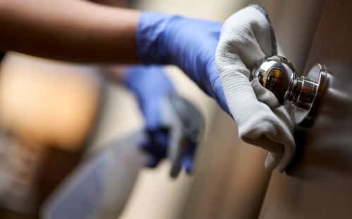 housemaid in protective gloves disinfecting the door handle in hotel 1