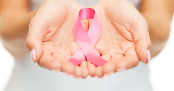 A pair of hands gently holding a pink ribbon, a symbol of breast cancer awareness, against a soft, out-of-focus background.