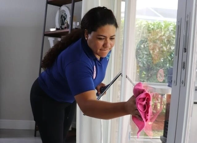 A uniformed worker uses a squeegee and pink cloth to clean a glass door, offering Cleaning services.