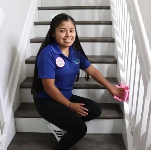 Smiling cleaning professional wiping a staircase railing, representing Yorleny's Cleaning Services.
