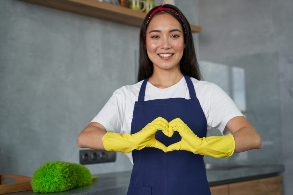 A smiling cleaner makes a heart with yellow gloves, showcasing Cleaning Trends 2025.