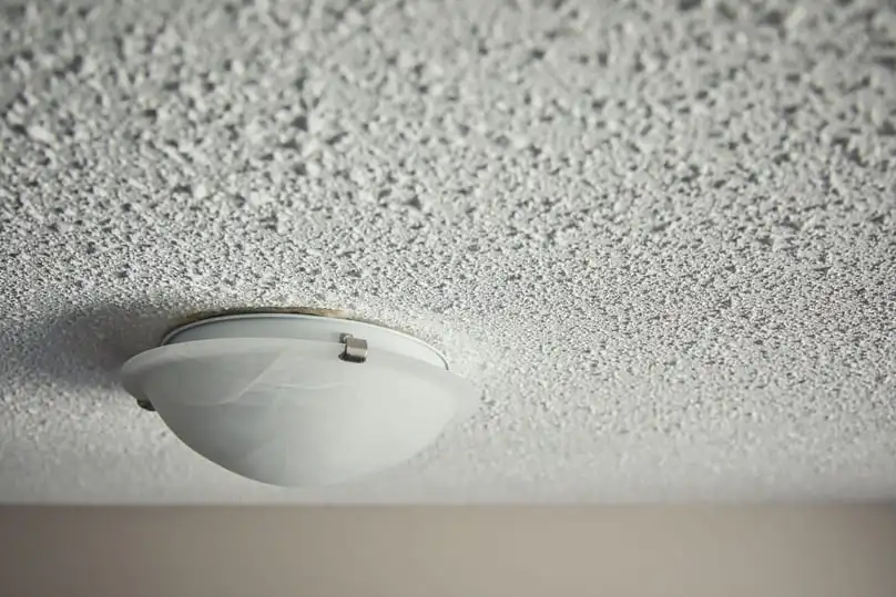 A popcorn ceiling with a light fixture, showing the need to know how to clean a popcorn ceiling.