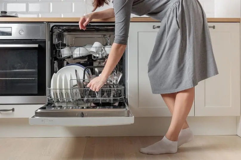 Woman unloading clean dishes from a dishwasher showing how to clean a smelly dishwasher