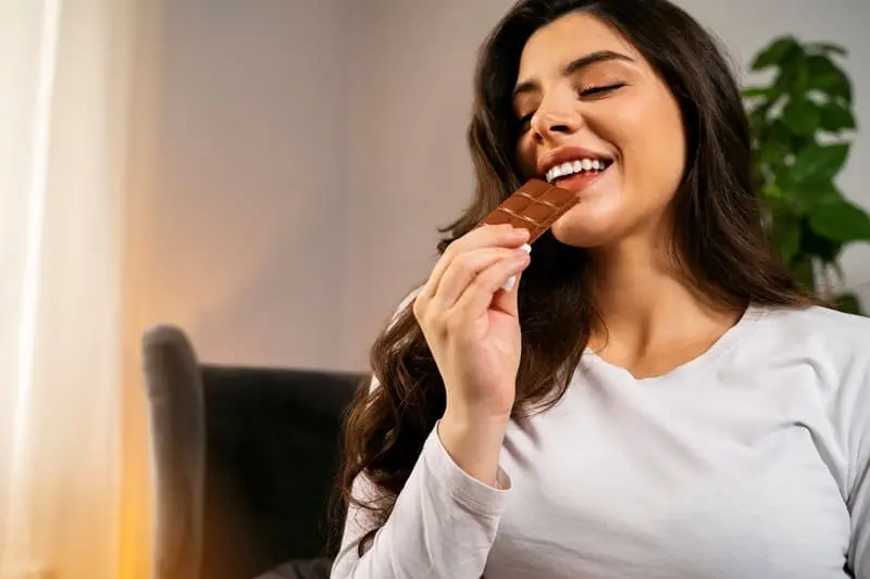 Woman enjoying a chocolate bar while sitting on a couch, a common scenario that can lead to accidental spills—learn how to get chocolate stains out of furniture safely and effectively.