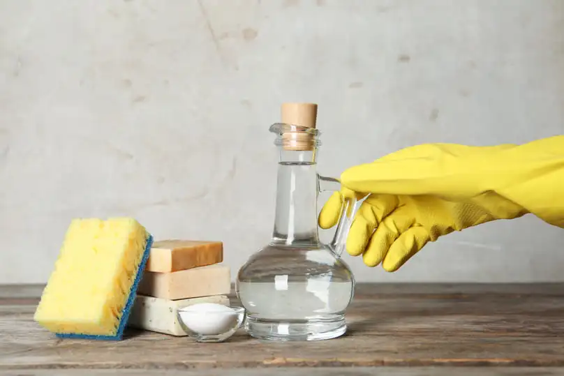 A gloved hand reaches for a bottle of vinegar, illustrating natural cleaning with vinegar.