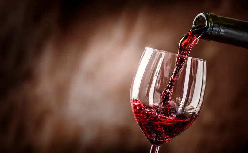 Red wine pouring into a glass, showing the need of knowing how to get red wine out of carpet.