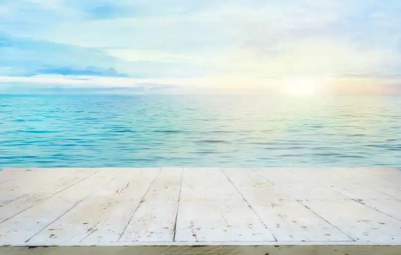 A white wooden deck overlooks a calm ocean, a peaceful sight after a summer cleaning checklist.