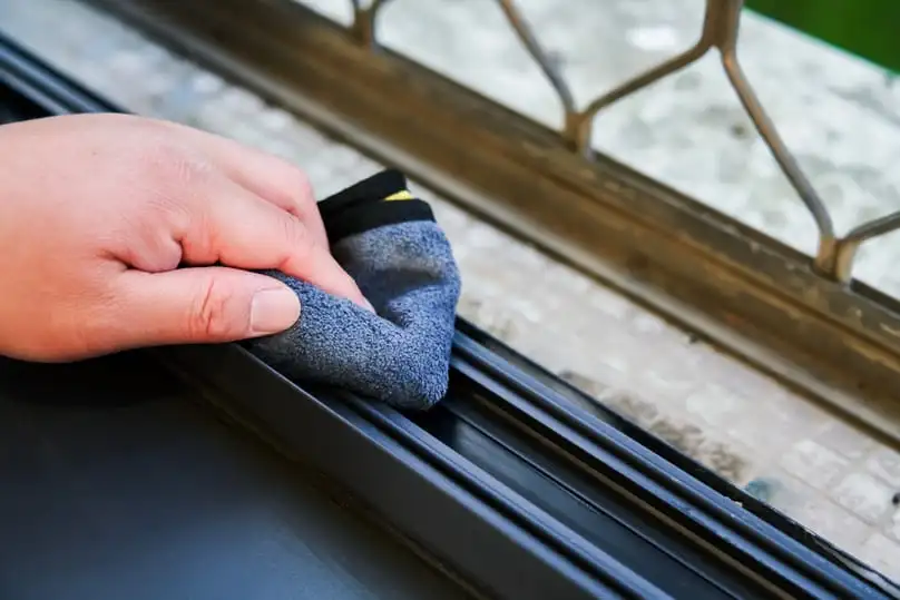 A hand cleaning the narrow track of a window with a cloth, demonstrating how to clean window tracks.