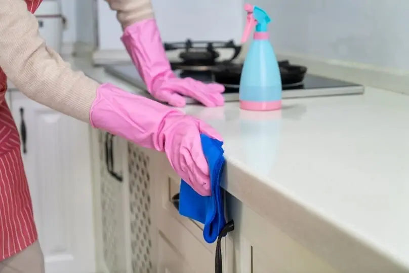 A professional in an apron wiping a kitchen countertop, showcasing house cleaning services.