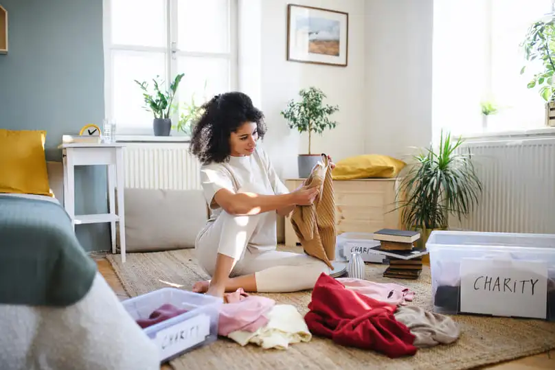 A woman sorting clothes into "charity" bins, a perfect example of how to declutter your home.