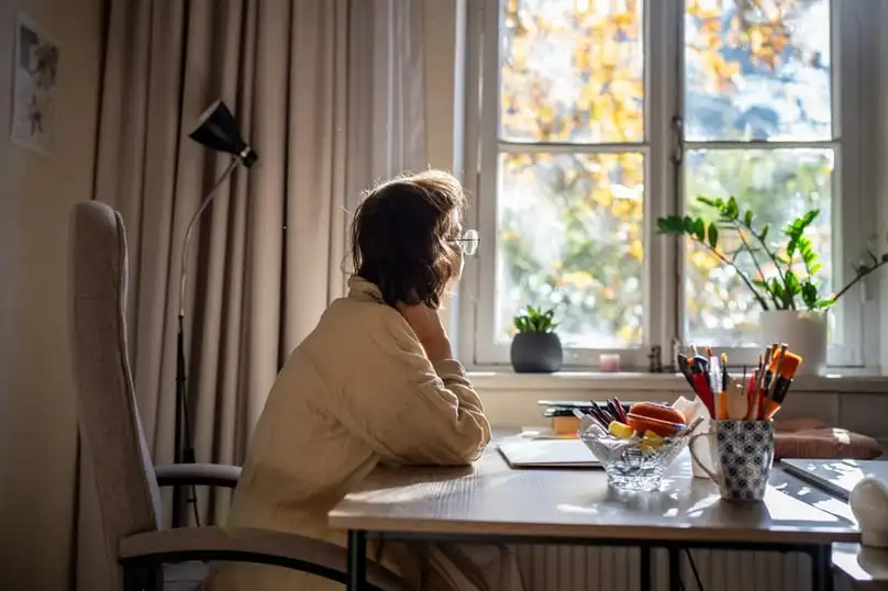A distracted individual sits by a window, needing an ADHD cleaning checklist to focus.