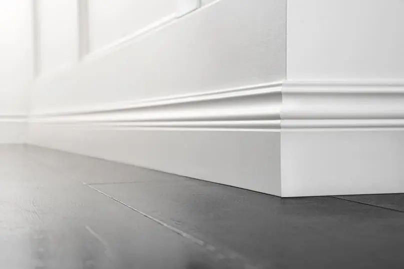Close-up of white baseboards and dark wood floor, guiding on how to clean baseboards.