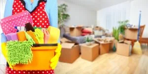 A cleaner with supplies stands before a room of moving boxes, defining what is professional move out cleaning.