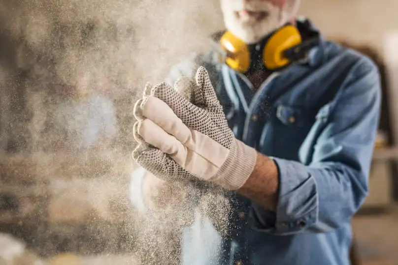 Worker wearing gloves surrounded by dust particles, illustrating how to clean up construction dust.