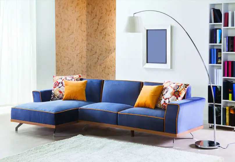 A blue microfiber sofa with orange & patterned cushions, suggesting how to clean a microfiber couch.